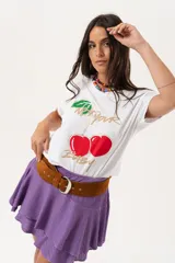 Remera blanca de algodón y elastano, con cuello redondo y mangas cortas. Estampado frontal con cerezas y texto en dorado.