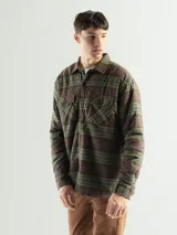 Sobrecamisa de franela a cuadros en tonos marrones y verdes, con forro interior de corderito, cierre frontal con botones y dos bolsillos en el pecho.