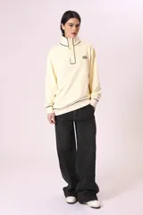 Buzo color crema con cuello alto abotonado y puños con ribete negro.