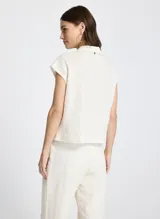 Chaleco color crudo de punto texturizado con sutil estampado a cuadros, corte recto, cuello, cierre de botones frontal, bolsillos frontales con botones y largo corto.