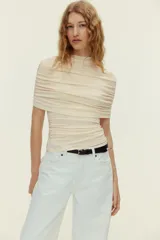 Top entallado de punto suave en color beige, con cuello tortuga, capa decorativa superpuesta y frunces laterales que generan un efecto drapeado.