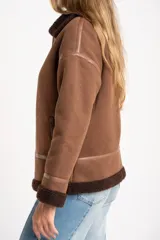 Chaqueta tipo gamulán de calce oversize en color marrón, con cuello y ribetes de corderito en contraste. Presenta cierre frontal de cremallera, bolsillos laterales y detalles de tiras decorativas en material sintético.