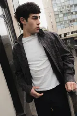 Camisa de corte boxy con estampado de cuadros pequeños en tonos oscuros. Presenta cuello camisero en color negro, cierre frontal con botones, canesú en la parte superior y un bolsillo en el pecho con etiqueta de la marca Kapsul Studio.