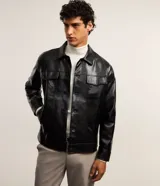 Campera trucker negra de cuero sintético con textura crocco, cuello inglés, cierre con botones, bolsillos con solapa en el pecho y puños abotonados.