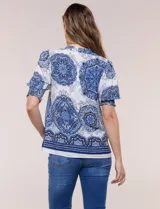 Blusa de crepe color blanco con estampado paisley en tonos azules y negros. Presenta cuello mao con escote en V, cierre frontal con botones y mangas cortas abullonadas con puños elastizados en punto smock.