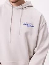 Canguro gris claro con capucha y estampado trasero en azul. El estampado incluye el texto "Spirit League Rusty Team" y una ilustración de una camioneta con animales y tablas de surf.