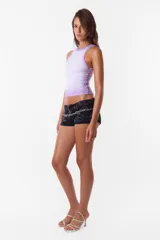 Microshort de gabardina de tiro bajo y corte slim fit. Presenta costuras en contraste color rojo, cierre metálico frontal y presillas largas en la cintura. La prenda cuenta con un proceso de sobreteñido y lavado artesanal que le otorga un aspecto desgastado único.