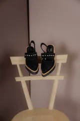 Zapatos tipo zueco de gamuza negra con punta fina y tira sobre el empeine decorada con tachas metálicas plateadas. Posee taco cuadrado de madera y suela con plataforma.