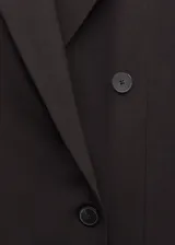 Blazer de corte sastre y diseño cruzado, con cierre de botones frontales, solapas clásicas y bolsillos laterales con solapa. Presenta una estructura entallada y hombros definidos.