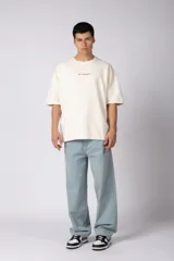 Remerón de corte oversized confeccionado en tejido rústico, con cuello redondo y mangas cortas. Presenta un diseño minimalista con una pequeña estampa frontal centrada en el pecho.
