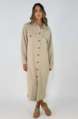Vestido camisero largo de color beige, con cierre frontal de botones, bolsillos con solapa en el pecho y mangas largas con puños.