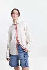 Camisa oversize color crema con detalles de puntilla roja en el frente.