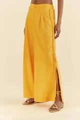 Pantalón amarillo de lino y viscosa, de pierna ancha, con cintura alta, pretina recta en la parte delantera y elástica en la parte trasera. Presenta detalle de trenza vertical en los laterales y aberturas en el dobladillo.