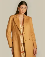 Gabardina larga color camel con diseño estructurado y tejido texturizado. Presenta hombros marcados, mangas largas con botones forrados y bolsillos decorativos.