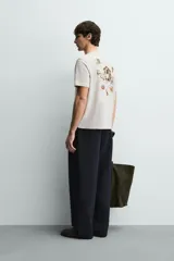 Camiseta de corte relajado, color gris jaspeado, con cuello redondo y manga corta. Presenta un parche rectangular azul marino en el centro del pecho con texto estampado en blanco y una frase adicional debajo.