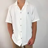Camisa de tejido de punto con textura, color blanco, de corte oversize, manga corta y cuello solapa. Presenta cierre frontal con botones y un pequeño bordado en el pecho.