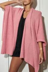 Ruana o poncho de tejido de punto abierto color rosado, con cuello chal y caída asimétrica.