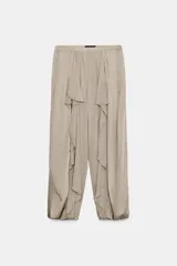 Pantalón bombacho de tiro medio en hilatura de viscosa color beige, con bolsillos laterales ocultos, volantes delanteros a tono, bajo abullonado con elástico y cierre lateral con cremallera oculta.
