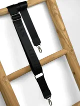 Correa ajustable para cartera confeccionada en cinta tejida con diseño de rayas en negro, blanco y beige, con punteras de cuero sintético negro y herrajes metálicos.