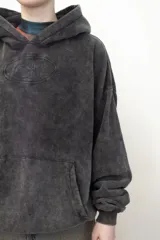 Canguro con capucha de calce holgado, confeccionado en tejido con efecto lavado ácido en color gris oscuro. Presenta un bordado tonal en el centro del pecho y un bolsillo frontal tipo canguro.