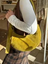 Cartera tipo hobo de gamuza color verde oliva, con cierre superior y correa ajustable al hombro.