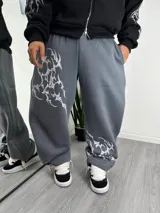 Pantalón de jogging gris de corte holgado, con estampado tribal en color blanco en la pierna derecha y en el tobillo izquierdo. Cuenta con cintura elástica y bolsillos laterales.