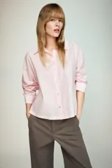 Camisa de popelín color rosa pálido, con cuello solapa, escote pico y manga larga terminada en puño. Cierre frontal con botones.