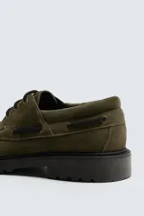 Zapato tipo náutico de hombre, confeccionado en piel con acabado de serraje en color verde oliva. Presenta cordonera con tres pasados, horma redonda y suela track dentada en color negro.