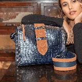 Cartera azul de cuero vacuno con textura tipo cocodrilo. Tiene un bolsillo con cierre en la tapa trasera y un cierre superior. Viene con una correa larga ajustable. El interior está forrado en tela y contiene un bolsillo para el móvil.