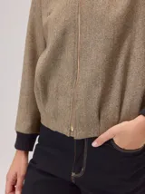 Chaqueta tipo bomber de lana con estampado de espiga en tonos grises. Presenta cuello, puños y ruedo en tejido elástico negro, cierre frontal dorado y bordado sutil en el pecho.