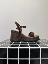 Sandalias de taco corrido color marrón, confeccionadas en cuero de gamuza con textura en la plataforma. Poseen tiras finas en la parte delantera y tira ajustable con hebilla en el tobillo.