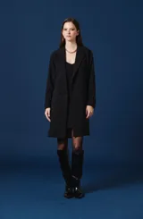 Saco largo tipo trench de color tostado, con diseño de doble botonadura, solapas clásicas y cinturón ajustable en la cintura. Presenta mangas largas con trabillas en los puños y una silueta estructurada y fluida.