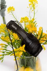 Sandalia de cuero color marrón, con tiras finas entrelazadas en el empeine y pulsera con cordón para anudar al tobillo. Tiene taco medio tipo carrete y punta cuadrada.