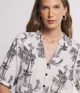 Camisa de viscolino Marfinno color beige con estampado de cocoteros en negro, cuello en V con escote hincapié y botones frontales negros. Mangas cortas con puños elásticos fruncidos.
