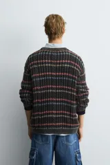 Jersey de punto con ajuste relajado, cuello redondo y manga larga. Presenta un diseño de rayas horizontales multicolores sobre una base oscura con textura de ochos y efecto lavado.