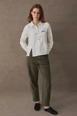 Remera estilo polo de manga larga, confeccionada en una mezcla de algodón y lino. Presenta un cierre frontal parcial, cuello camisero y aberturas laterales en el frente. El diseño incluye un estampado integral con motivos deportivos y un detalle bordado en el pecho.