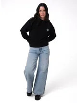 Buzo de cuello redondo color negro, con calce holgado y mangas largas. Presenta un estampado gráfico en el pecho con forma de corazón y la palabra 'Caterpillar', además de una etiqueta con el logo de la marca en el puño izquierdo. Posee puños, cuello y ruedo acanalados.