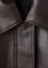 Chaqueta estilo bomber de cuero sintético en color marrón oscuro, con cuello camisero, cierre frontal de cremallera y botones a presión, bolsillos de parche con solapa y bajo elástico.