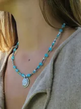 Collar corto confeccionado con cuentas de cristal facetadas en tonos multicolor, con un dije metálico colgante con relieve en forma de escudo y placa con marca grabada.