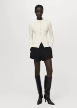 Cardigan de tejido de punto fino color blanco, con cuello redondo, manga larga y cierre frontal abotonado con diseño entallado.