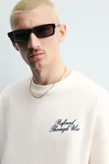 Camiseta blanca de corte relajado, con cuello redondo, manga corta y texto estampado en contraste en el pecho.