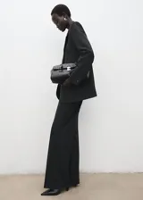 Pantalón de traje de tiro medio, color negro, de diseño recto y largo, con cierre frontal de cremallera, botón y ganchos ocultos con tapeta, y bolsillos laterales.