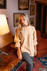 Blusa color beige de corte holgado, cuello alto con volados y mangas largas abullonadas con elástico en los puños.