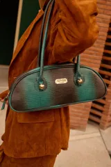 Cartera estilo baguette de cuero con textura tipo reptil en degradé de verde y negro. Presenta una silueta alargada y estructurada, con manijas largas y detalles de nudos esféricos metálicos en la unión de las mismas. Incluye placa metálica con logo de la marca en el frente.