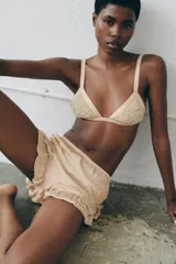 Shorts satinados color beige, con tiro medio, cintura elástica y diseño fluido. Presentan bordados florales en los laterales y volantes con puntillas en el bajo.