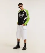 Bermuda ancha tipo baggy de sarga de algodón, color blanco, con cierre tradicional, bolsillos y detalle de cadena metálica colgante.