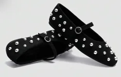 Balerinas negras de cuero sintético con tachas doradas, tira sobre el empeine con hebilla dorada y punta redondeada.