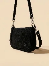 Cartera pequeña tipo bandolera confeccionada en gamuza color marrón oscuro, con cierre superior metálico y correa ajustable con herrajes plateados. Presenta un detalle de logo grabado en la parte inferior.