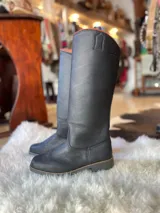 Botas altas de cuero color negro, de caña alta y diseño clásico, con suela plana y costuras visibles.