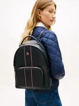 Mochila de poliuretano texturizado en color azul marino, con diseño curvo, bolsillo frontal con cierre y detalles de franjas verticales con los colores distintivos de la marca. Cuenta con el monograma TH metálico en dorado, cierre de cremallera superior, asa de mano y correas ajustables para la espalda.